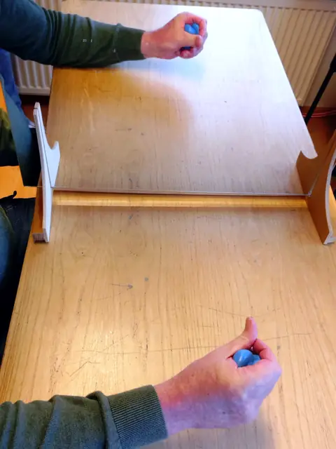 Spiegeltherapie: Die Hand drückt blaue Therapieknete zusammen, das Spiegelbild zeigt dieselbe Bewegung